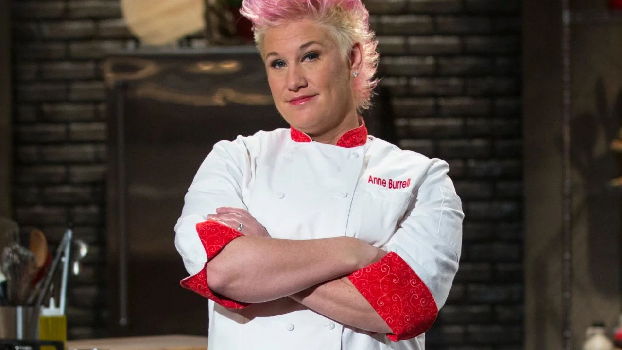 Anne Burrell smiling in chef coat on Food Network set